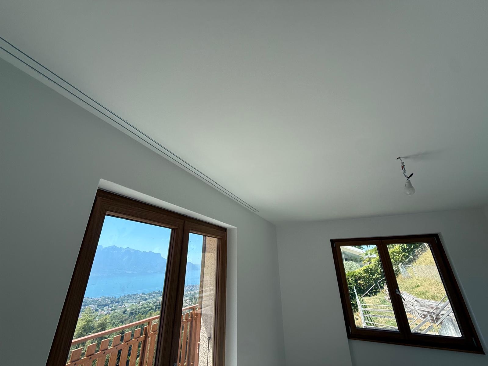 Chambre rénovée à Blonay : plafond et murs peints, fenêtres bois vue lac