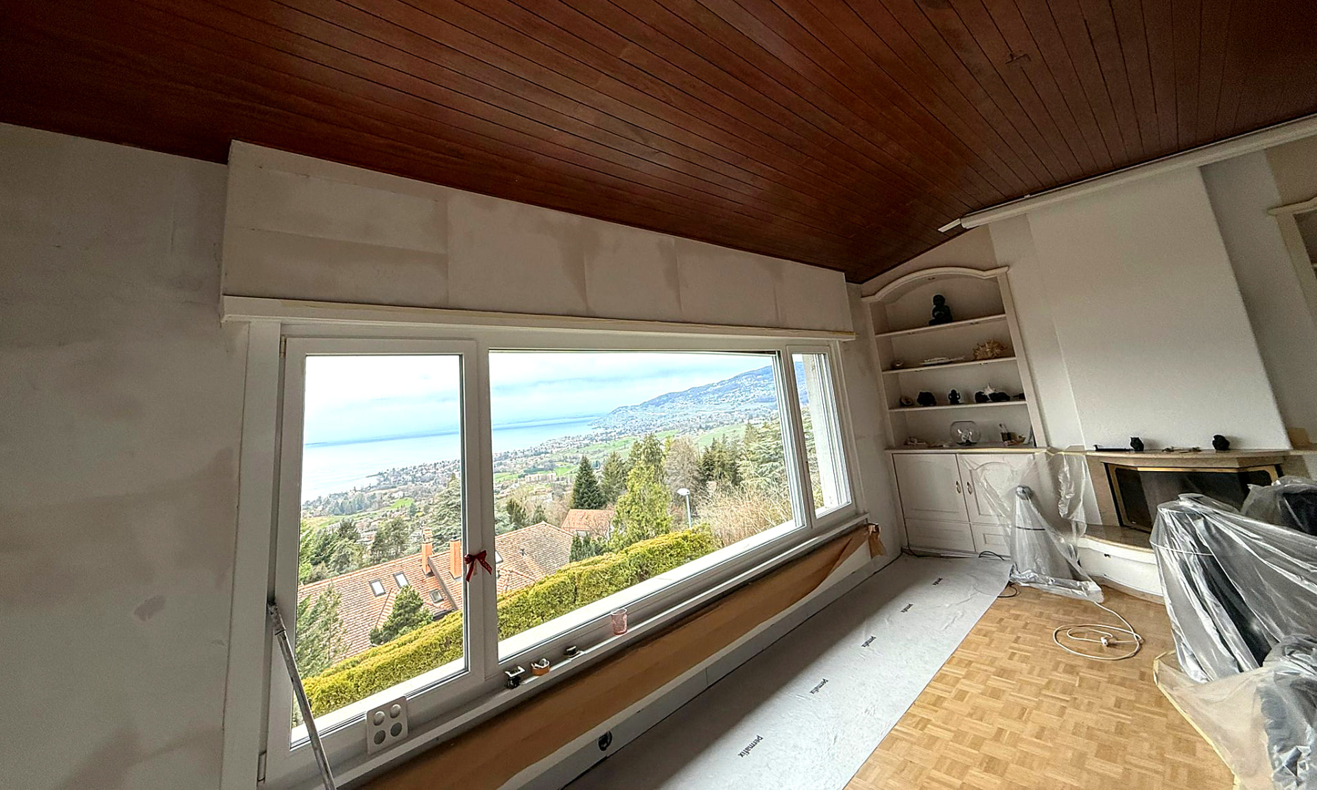 Salon en cours de rénovation à Brent : murs préparés et baie vitrée avec vue sur le lac Léman